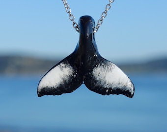 May include: A black and white whale tail pendant necklace. The tail is made of ceramic and has a glossy finish. The necklace is on a silver chain.