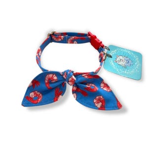 May include: Blue pet collar with a red shrimp pattern and a bow tie. The collar has a red plastic clasp and a tag with a cat illustration.