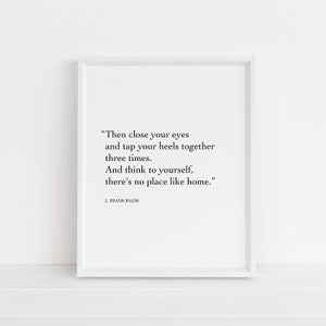 May include: A white framed print with a black and white quote from L. Frank Baum: "Then close your eyes and tap your heels together three times. And think to yourself, there's no place like home."