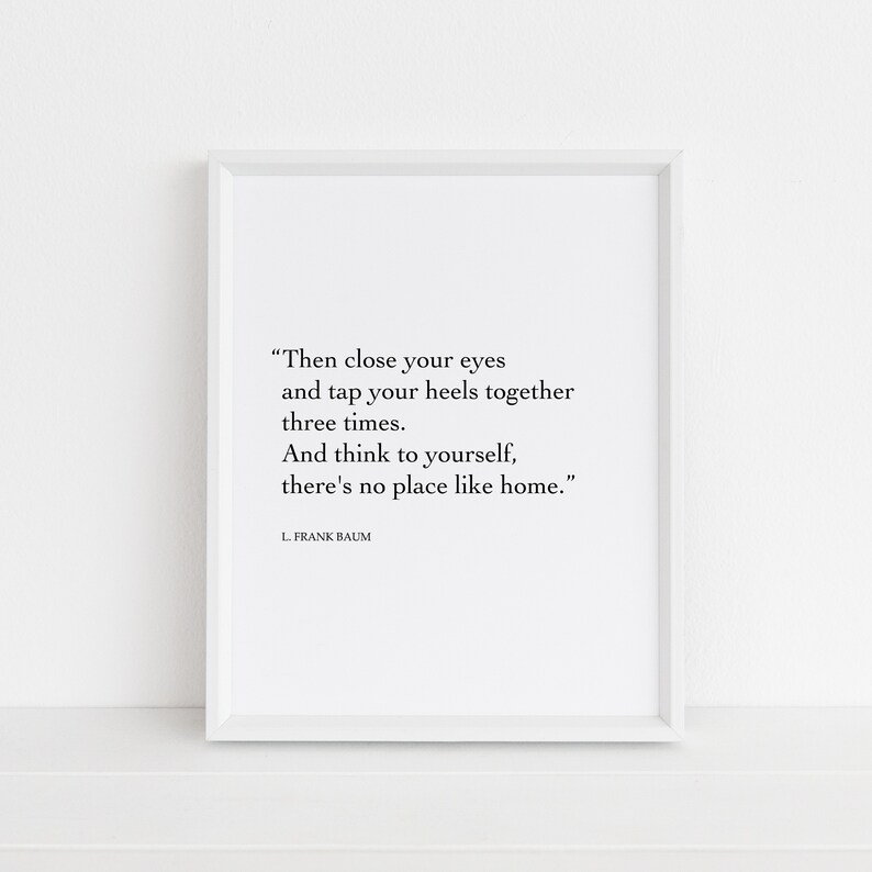 May include: A white framed print with a black and white quote from L. Frank Baum: "Then close your eyes and tap your heels together three times. And think to yourself, there's no place like home."