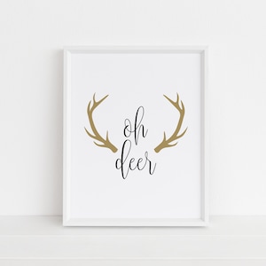 May include: White framed print with the text "oh deer" in black cursive font and a pair of gold antlers above the text.
