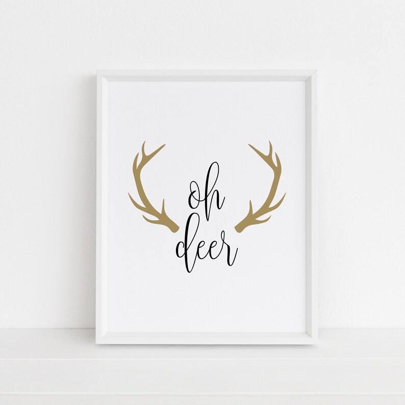 May include: White framed print with the text "oh deer" in black cursive font and a pair of gold antlers above the text.