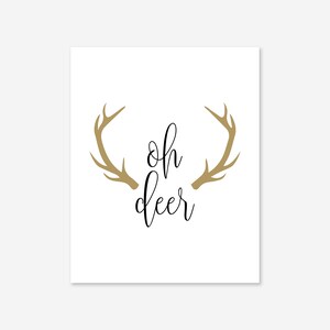 May include: A white background with a gold silhouette of a deer's antlers and the text "oh deer" in black cursive font.