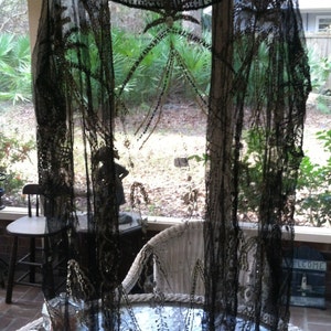 Könnte beinhalten: Ein schwarzer, perlenbesetzter Spitzen-Schal mit einem zarten Muster. Der Schal ist über einen Stuhl und einen Tisch gelegt, mit einem Fenster im Hintergrund.