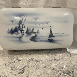 May include: White enamel bread box with a blue and white Dutch scene of a windmill, houses, and a sailboat on a lake.