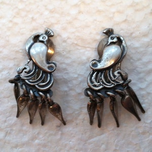May include: A pair of silver tone clip-on earrings featuring a bird design with a pearl-like center and dangling teardrop-shaped accents.