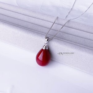 May include: A silver chain necklace with a red teardrop pendant. The pendant is made of a smooth, polished stone.