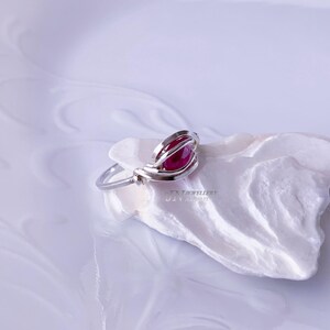 May include: A silver ring with a red gemstone set in a wire cage design.