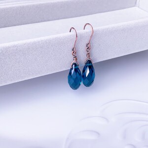 May include: A pair of copper wire earrings with teardrop-shaped blue crystal beads.