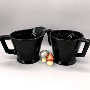 May include: A white ceramic mug with a black handle and the text "But First, Coffee" in a black, bold font. The mug is on a white surface.