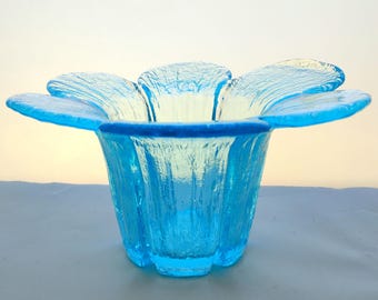 May include: A turquoise glass flower-shaped bowl. The bowl has a textured surface and a dark blue rim. The petals of the flower extend outwards, creating a unique and decorative design. The bowl is likely used for display or as a decorative piece.