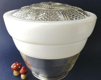 May include: A glass light fixture shade featuring a clear, textured top with a geometric pattern, a smooth white milk glass middle section, and a clear ribbed glass base. Two small red and white mushroom-shaped decorative items are placed nearby.
