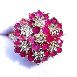 May include: A gold ring featuring a cluster of red rubies and white diamonds set in a flower design.