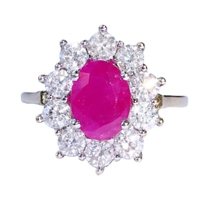 May include: A silver ring with a central oval ruby, encircled by a halo of smaller, round diamonds. The ruby is a vivid pink-red hue, and the diamonds are clear and sparkling. The ring's design is classic and elegant, suitable for various occasions.