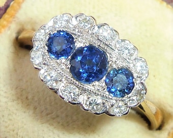May include: A vintage ring with three blue sapphires and a halo of diamonds set in white gold.