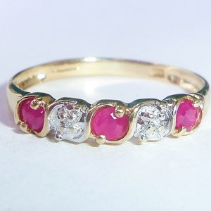 May include: A gold band ring with five stones. The ring has three red ruby stones and two smaller white diamond stones.