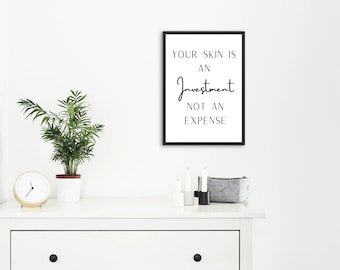 May include: Black and white framed print with the text "Your skin is an investment not an expense". The print is hanging on a white wall above a white dresser with a plant, a clock, and decorative items.