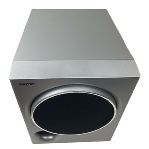 Pu&ograve; includere: Un subwoofer Sony argentato con una griglia per altoparlanti nera. Il subwoofer ha una parte anteriore arrotondata e una forma rettangolare.