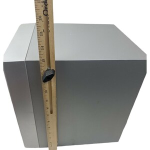 Pu&ograve; includere: Un altoparlante grigio con un righello di legno che misura 40,6 cm di altezza. L'altoparlante ha una forma rettangolare con bordi arrotondati.