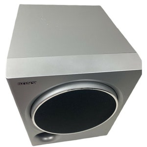 Pu&ograve; includere: Un subwoofer Sony argentato con una griglia dell'altoparlante nera. Il subwoofer ha un fronte arrotondato e una forma rettangolare.