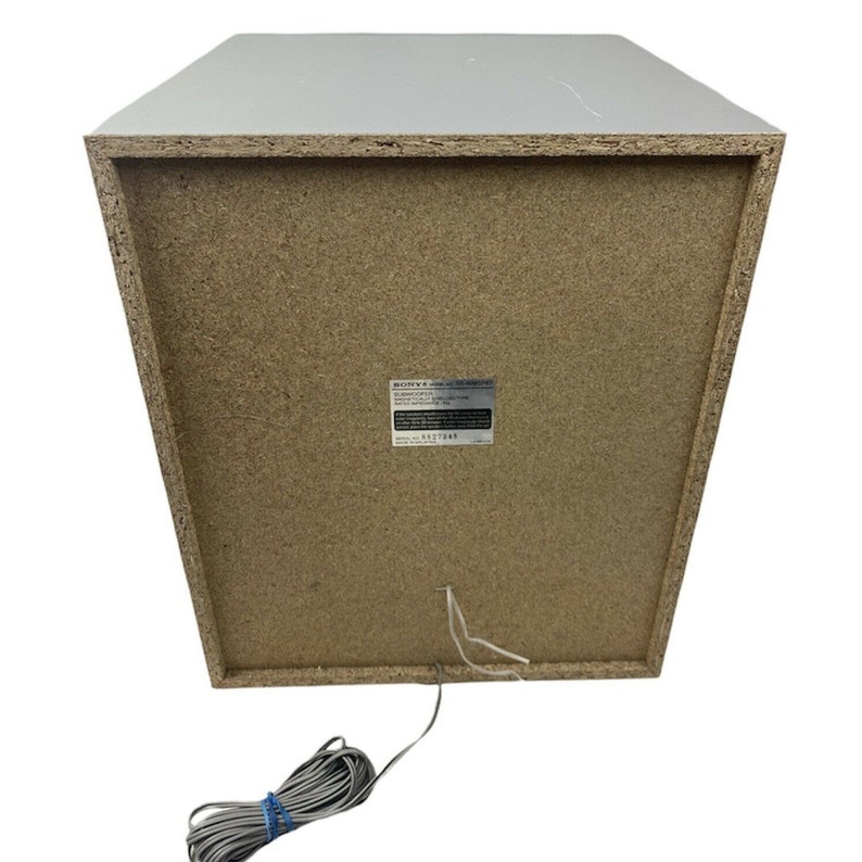 Pu&ograve; includere: Un subwoofer Sony bianco con una griglia dell'altoparlante marrone e un'etichetta sul retro che recita "Sony 5.1ch Home Theater System". Il subwoofer ha un filo grigio.