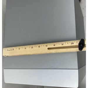 Pu&ograve; includere: Un altoparlante color argento con un righello di legno lungo 25,4 cm posizionato sopra l'altoparlante.