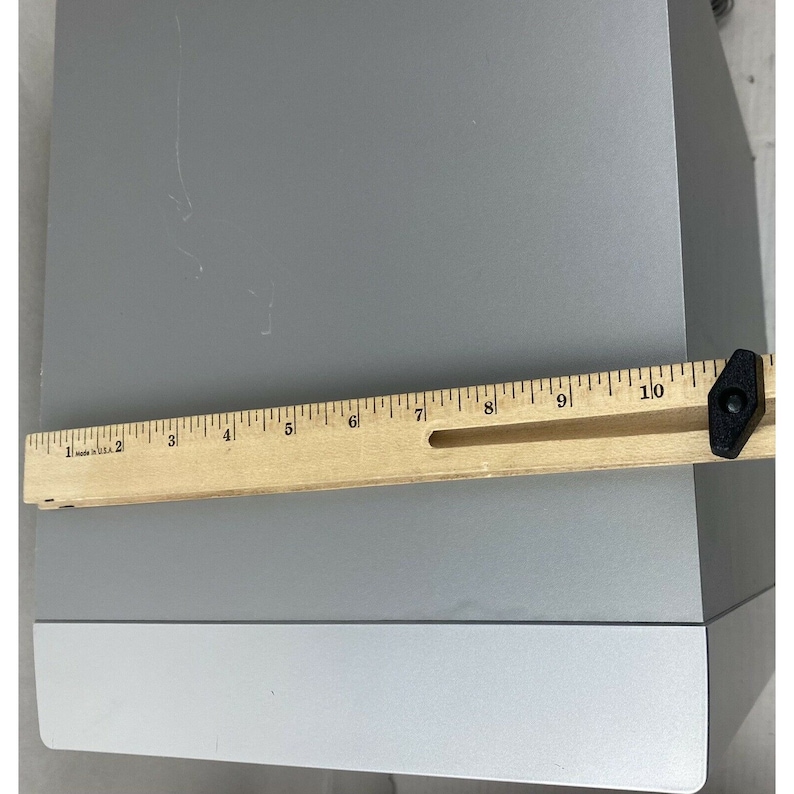 Pu&ograve; includere: Un altoparlante color argento con un righello di legno lungo 25,4 cm posizionato sopra l'altoparlante.