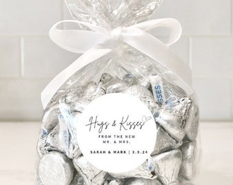 May include: A clear plastic bag filled with silver foil-wrapped chocolate kisses. A white round sticker with the text "Hugs & Kisses from the new Mr. & Mrs. Sarah & Mark | 3.9.24" is attached to the bag.