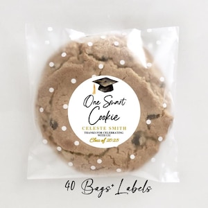 May include: A chocolate chip cookie in a clear cellophane bag with white polka dots. The cookie has a round label that reads "One Smart Cookie" with a graduation cap graphic. The text also includes "Celeste Smith" and "Class of 2025".