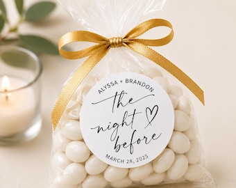 Peut inclure: Un sachet transparent rempli d'amandes dragéifiées blanches, noué avec un ruban de satin doré. Une étiquette ronde blanche sur le devant porte le texte "Alyssa + Brandon", "the night before", un cœur et "March 28, 2025".