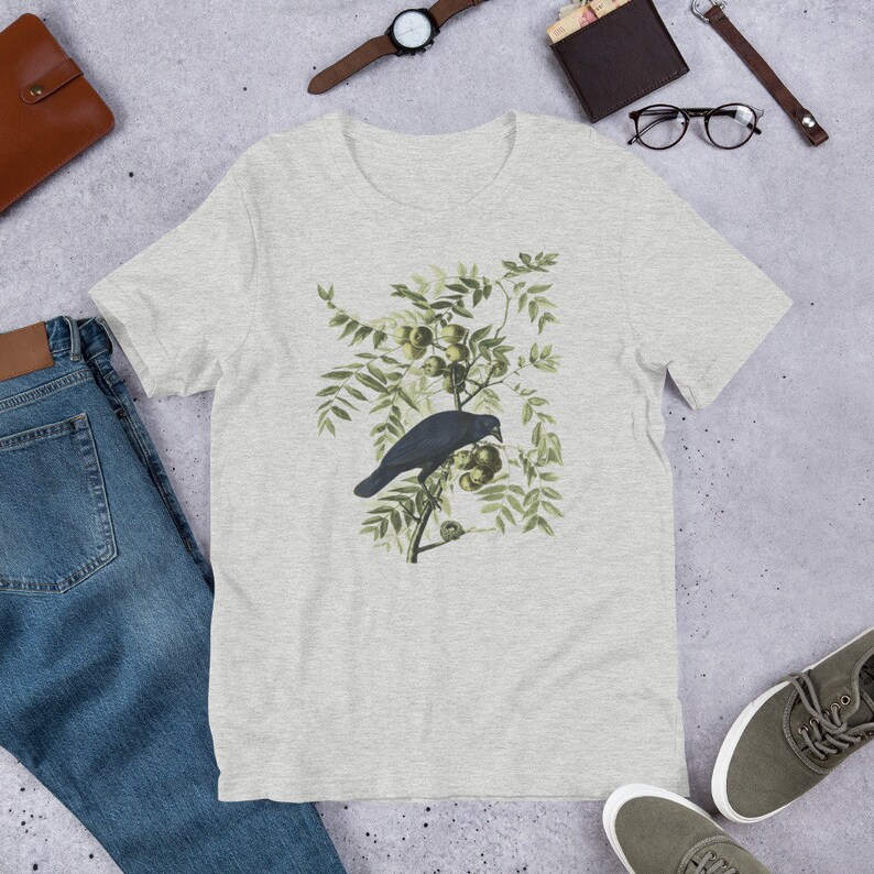 May include: A heather grey t-shirt with a vintage illustration of a black crow perched on a branch with green leaves and berries.