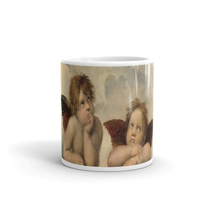 Puede incluir: Una taza de cerámica blanca con una imagen colorida de dos querubines con alas. Los querubines miran hacia arriba y tienen una expresión pensativa en sus rostros.