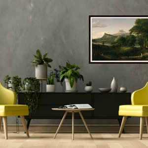 May include: A framed landscape painting depicting a mountain range with a lake in the foreground. The painting is in a brown frame and is hanging on a gray wall. There are two yellow chairs and a coffee table in front of the painting.