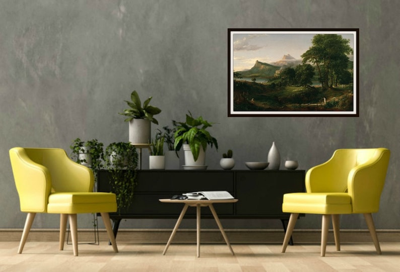 May include: A framed landscape painting depicting a mountain range with a lake in the foreground. The painting is in a brown frame and is hanging on a gray wall. There are two yellow chairs and a coffee table in front of the painting.