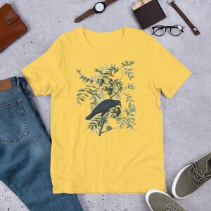May include: A yellow short-sleeved t-shirt with a vintage illustration of a black crow perched on a branch with green leaves and berries.