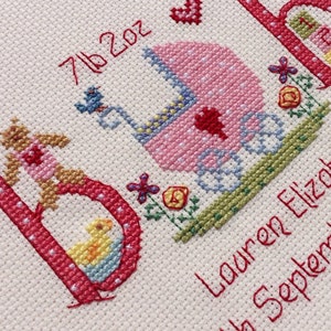 May include: Cross-stitch embroidery with the letters 'B' and 'A' in pink and red, a pink baby carriage, and the text '7th 202' and 'Lauren Eliza 4th September'.