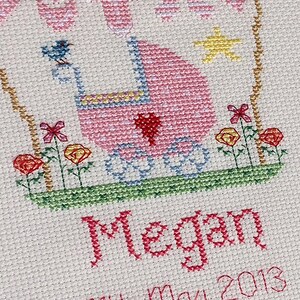 May include: Pink and blue cross-stitch embroidery with a baby carriage, flowers, and the name Megan and the date May 2013.