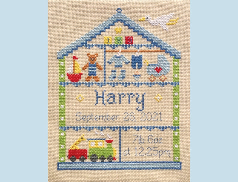 Puede incluir: Un dise&ntilde;o de punto de cruz de una casa azul con un p&aacute;jaro blanco en el techo. La casa est&aacute; llena de art&iacute;culos para beb&eacute;s, incluyendo un osito de peluche, un velero, un cochecito y un tren. El nombre "Harry" est&aacute; bordado debajo de la casa, junto con la fecha "26 de septiembre de 2021" y el peso y la hora de nacimiento: "7lb 6oz a las 12:25pm".