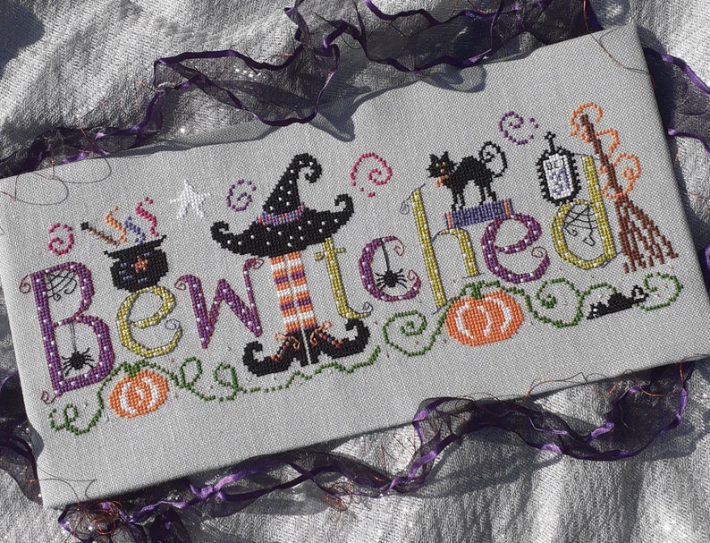 May include: Cross stitch pattern featuring the word "Bewitched" with a witch, a black cat, a cauldron, a broom, and pumpkins.