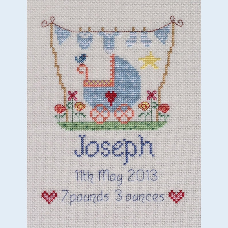 May include: A blue and white baby carriage with a red heart, surrounded by flowers, with the name Joseph, the date 11th May 2013, and the weight 7 pounds 3 ounces.