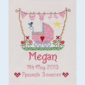 May include: Pink and white cross-stitch embroidery with a baby carriage, a bird, and a sun. The text reads "Megan", "11th May 2013", and "7 pounds 3 ounces".