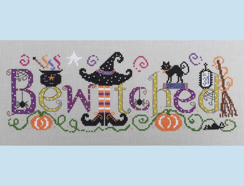 May include: Cross-stitch embroidery design featuring the word "Bewitched" with a witch, a black cat, a cauldron, pumpkins, and a broom. The design is on a gray background with white polka dots.
