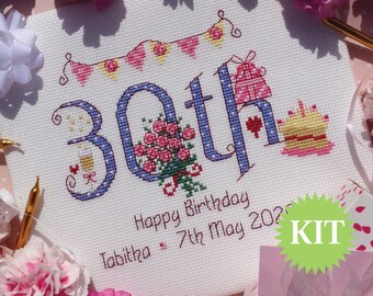 May include: Cross stitch kit for a 30th birthday with a blue and white polka dot background. The kit includes a design with the number 30, a bouquet of roses, a birthday cake, a gift, and a glass of champagne. The text "Happy Birthday Tabitha 7th May 2023" is included in the design.