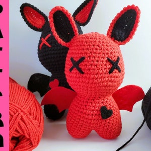 Könnte beinhalten: Zwei gehäkelte Amigurumi-Spielzeuge in Form von Fledermäusen aus rotem und schwarzem Garn. Die Fledermäuse haben gestickte Augen und Münder, und eine Fledermaus hat ein schwarzes Herz auf der Brust.