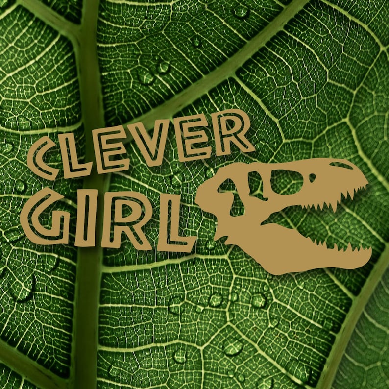 May include: A green leaf with a brown dinosaur skull and the text "CLEVER GIRL" in brown outlined letters.