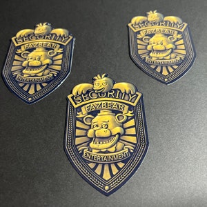 May include: Three gold and black security badges with the text "SECURITY FAZBEAR ENTERTAINMENT" and a cartoon bear face.