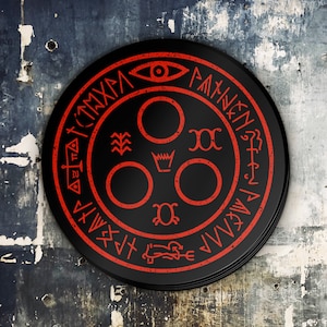 Puede incluir: Un s&iacute;mbolo circular negro y rojo con un ojo estilizado, una corona y otros s&iacute;mbolos. El s&iacute;mbolo est&aacute; rodeado por un anillo de texto en una fuente estilizada.