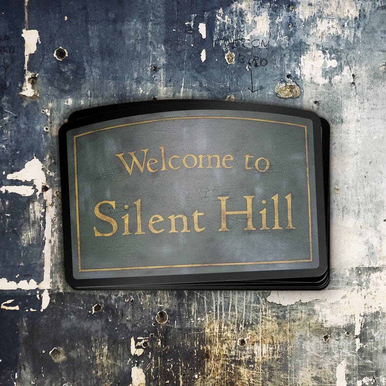 Puede incluir: Un letrero negro con la parte superior curvada y un fondo verde oscuro. El letrero dice "Bienvenido a Silent Hill" en letras doradas.