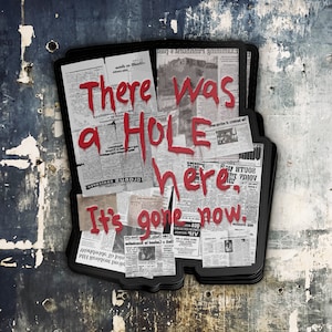Puede incluir: Una pila de peri&oacute;dicos viejos con las palabras "There was a HOLE here. It's gone now." escritas en pintura roja.