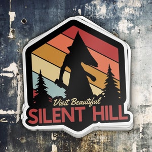 Puede incluir: Una pegatina de estilo retro con la silueta de una figura que lleva una cabeza en forma de pir&aacute;mide, de pie frente a un fondo de colores de puesta de sol con &aacute;rboles a cada lado. El texto "Visit Beautiful Silent Hill" est&aacute; impreso debajo de la figura.
